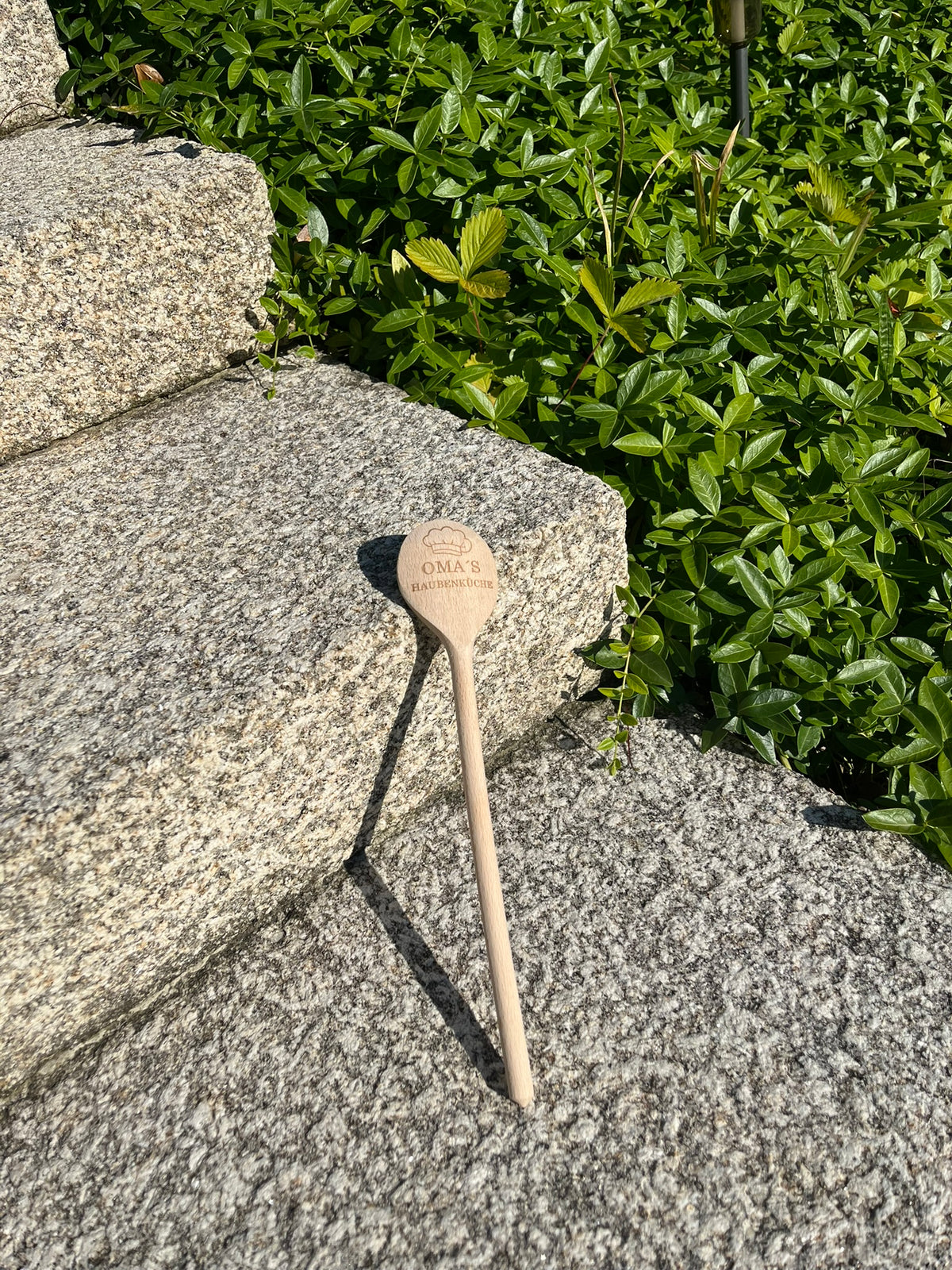 Gravierter Kochlöffel aus Holz an einer Steinstufe lehnend