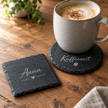 Runder Schiefer-Untersetzer mit Gravur „Kaffeezeit“ unter einer Tasse und eckiger Untersetzer mit Namen „Anna“